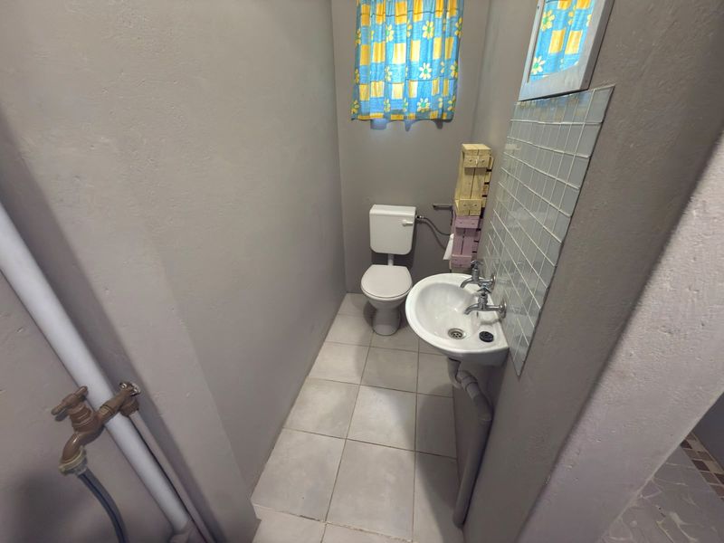 A compact bathroom featuring a pedestal basin with tiled splashback and a standard toilet, finished with neutral wall paint and floor tiles.