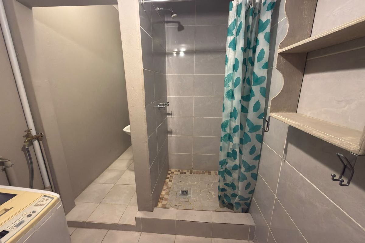 A functional bathroom featuring a tiled shower enclosure, tiled flooring, and built-in wall shelving, requiring some maintenance and cosmetic updates.