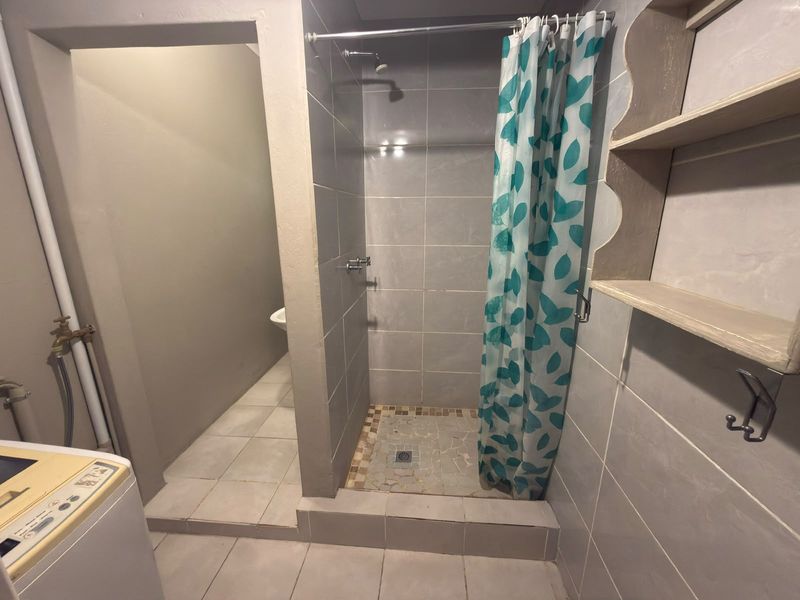 A functional bathroom featuring a tiled shower enclosure, tiled flooring, and built-in wall shelving, requiring some maintenance and cosmetic updates.