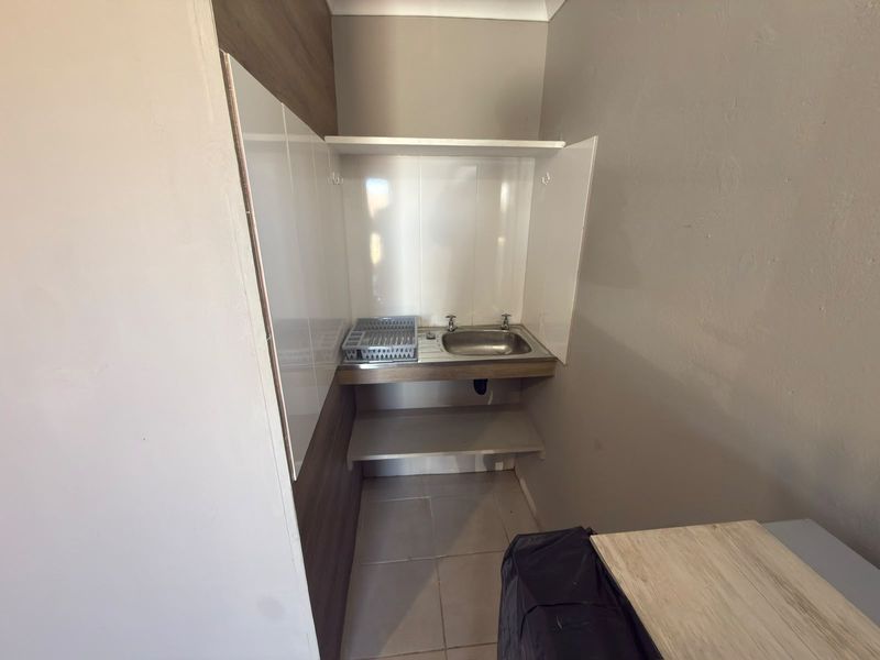 A compact scullery or utility area featuring a stainless steel sink, tiled splashback, and built-in shelving, providing a functional space for cleaning and storage.