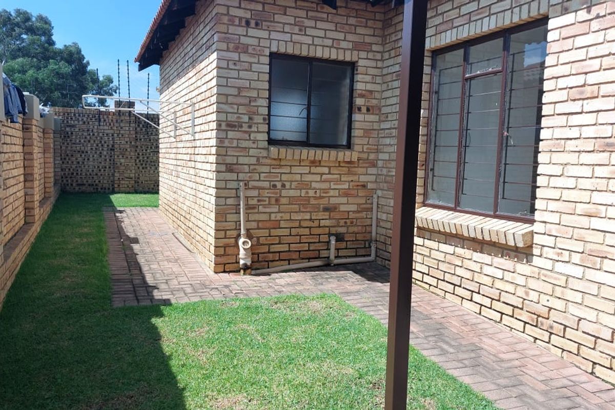 A private rear garden area featuring a paved walkway, face brick exterior walls, and secure perimeter fencing.