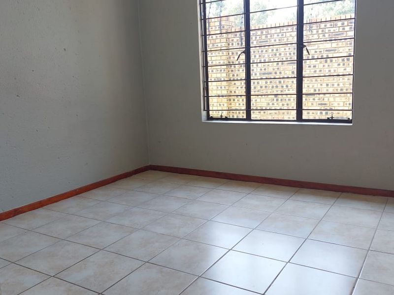 An empty bedroom featuring tiled flooring and a window fitted with security bars, offering a neutral blank canvas for potential buyers.