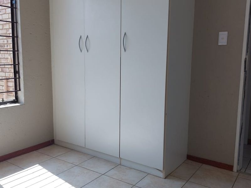 A simple bedroom featuring tiled flooring, a built-in wardrobe, and a window with security bars.