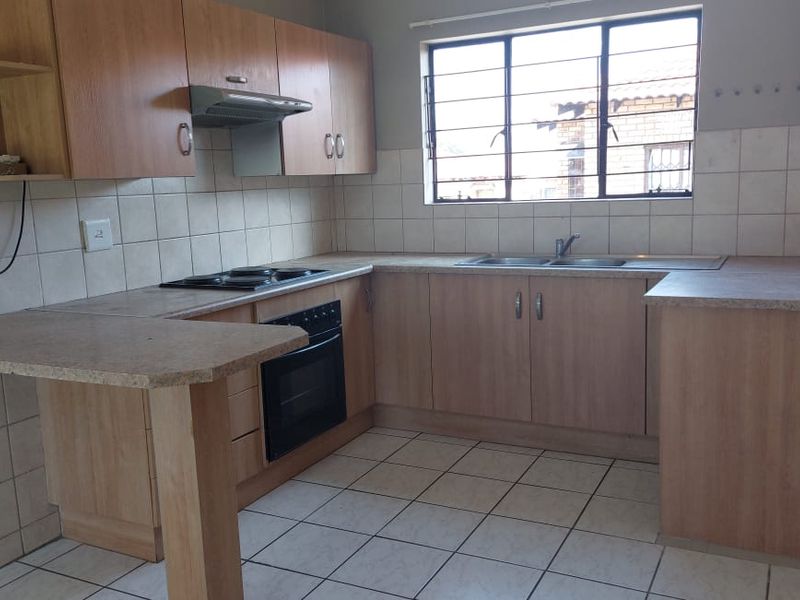 A functional kitchen featuring laminate cabinetry, built-in oven with hob, extractor fan, double bowl sink, and tiled flooring with security bars on the window.
