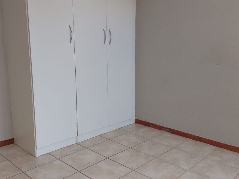 A vacant bedroom featuring neutral wall paint, tiled flooring, and a built-in white wardrobe.