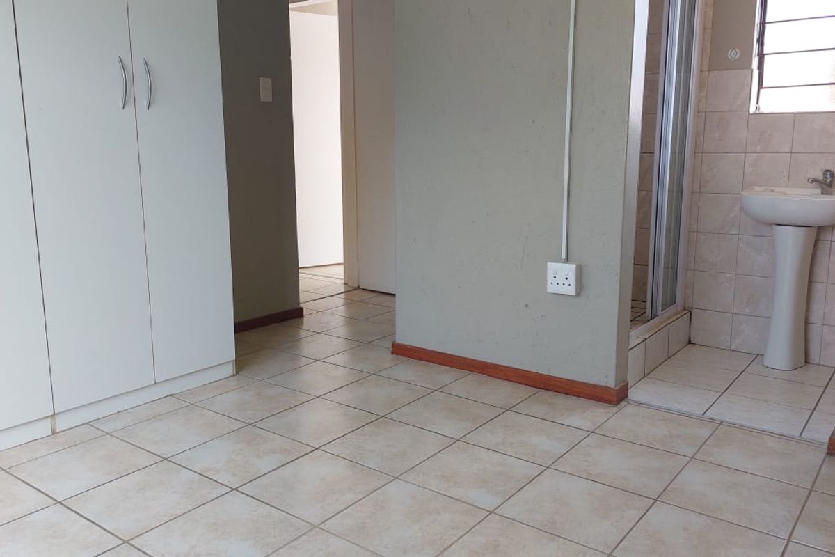 A functional bedroom featuring tiled flooring, built-in cupboards, and an en-suite shower and basin area.