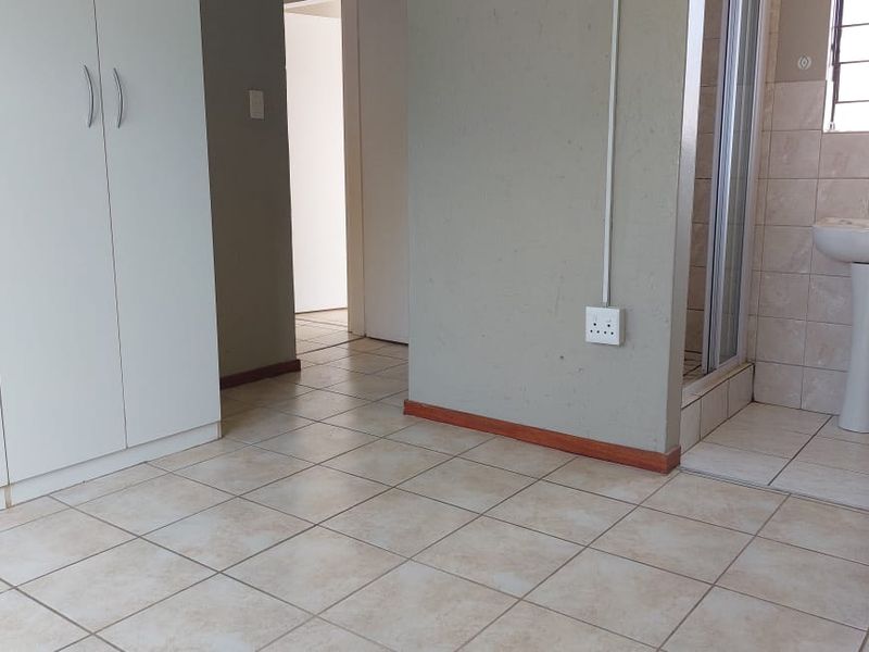 A functional bedroom featuring tiled flooring, built-in cupboards, and an en-suite shower and basin area.