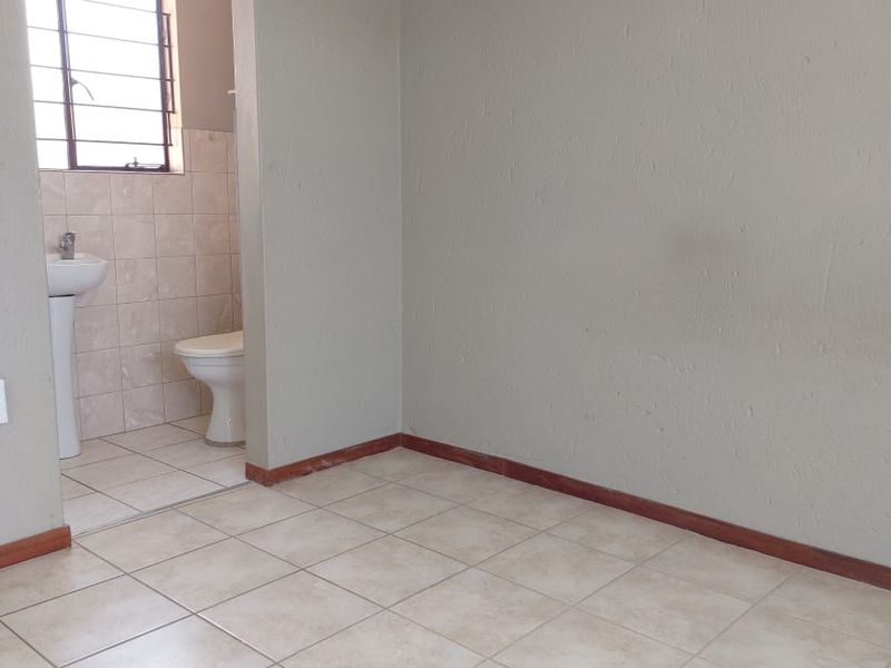 A functional, empty bathroom featuring a pedestal basin, toilet, and neutral ceramic floor tiles with a tiled splashback area.