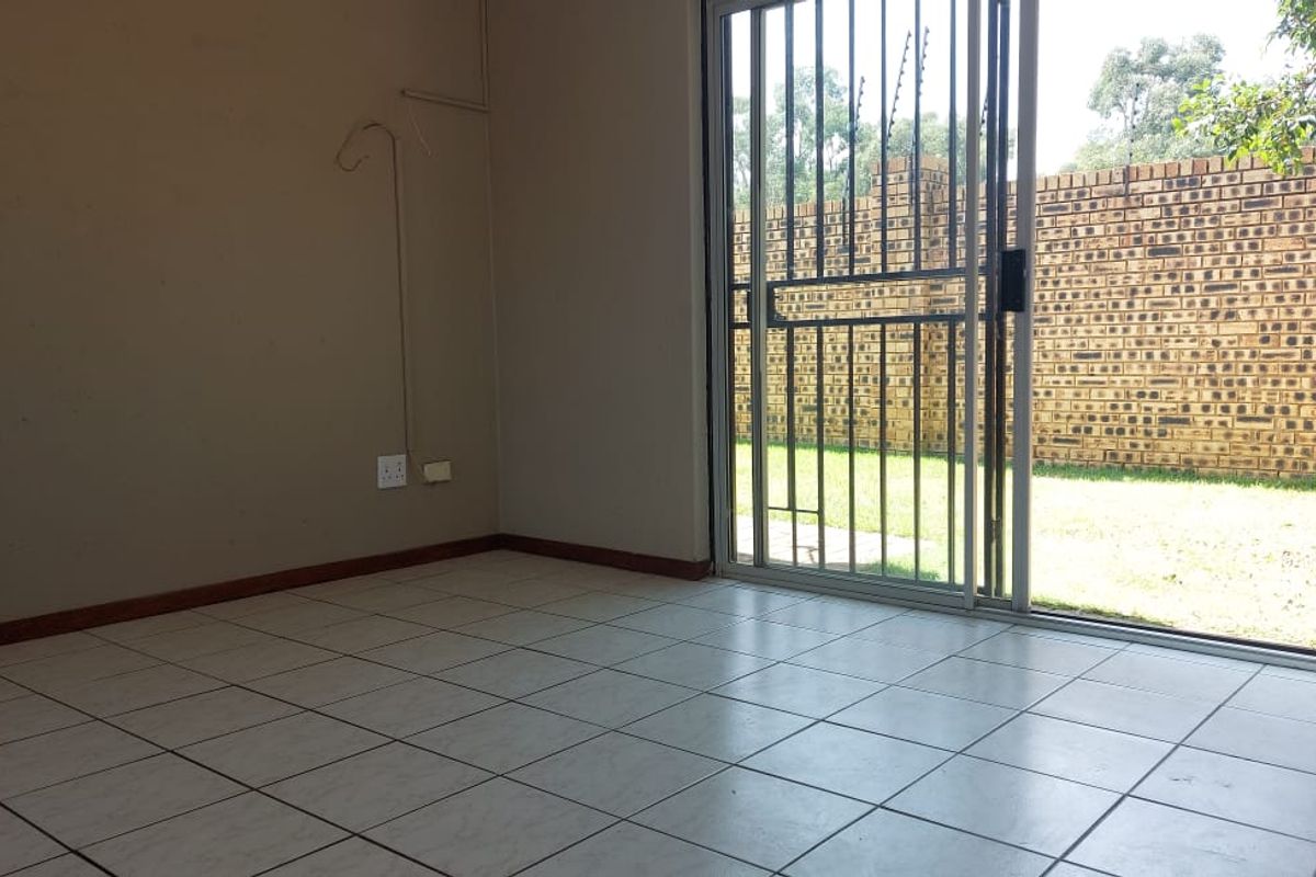 An empty living room featuring tiled flooring and a sliding glass door with a security gate, providing direct access to the rear garden.