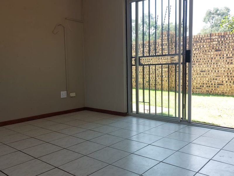 An empty living room featuring tiled flooring and a sliding glass door with a security gate, providing direct access to the rear garden.