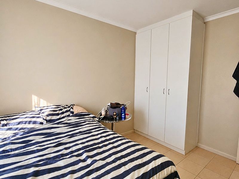 A bedroom featuring neutral wall tones, tiled flooring, and a white built-in wardrobe providing ample storage space.