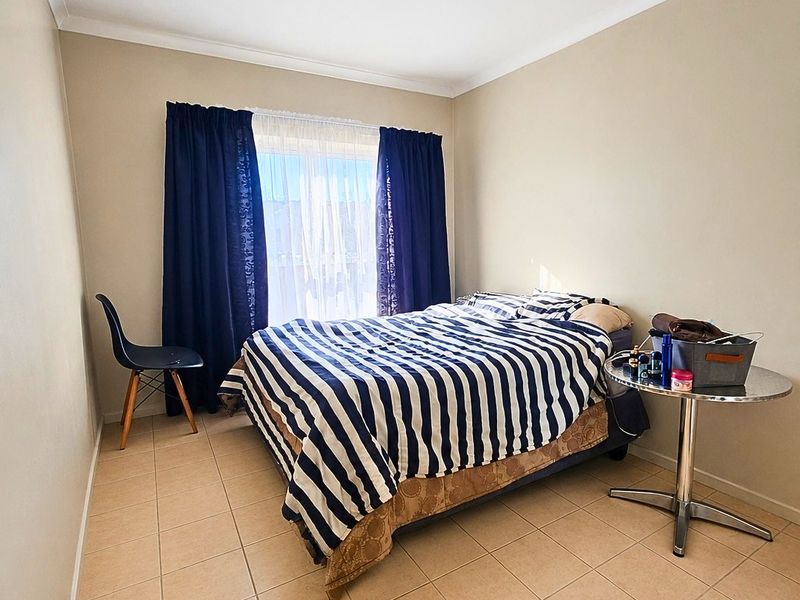 A functional bedroom featuring neutral wall tones, tiled flooring, and a coved cornice, providing a clean and simple living space.