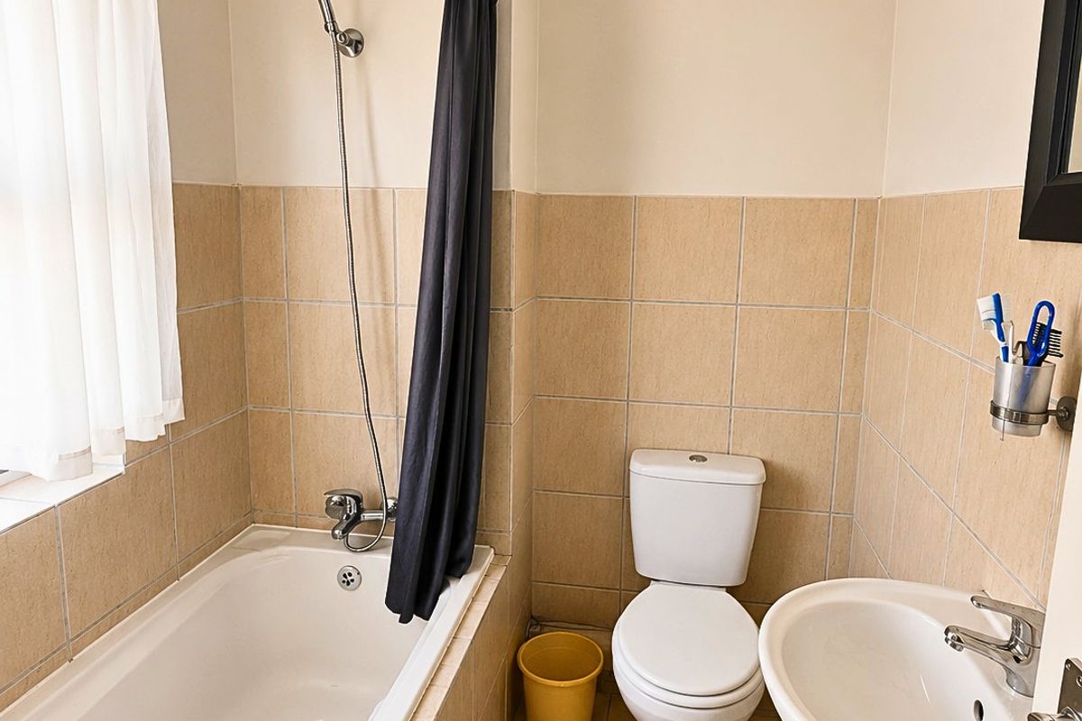 A functional bathroom featuring a bathtub with shower attachment, a pedestal basin, and a toilet, finished with neutral wall and floor tiling.