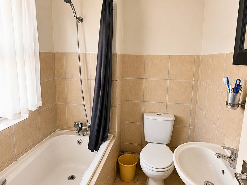 A functional bathroom featuring a bathtub with shower attachment, a pedestal basin, and a toilet, finished with neutral wall and floor tiling.