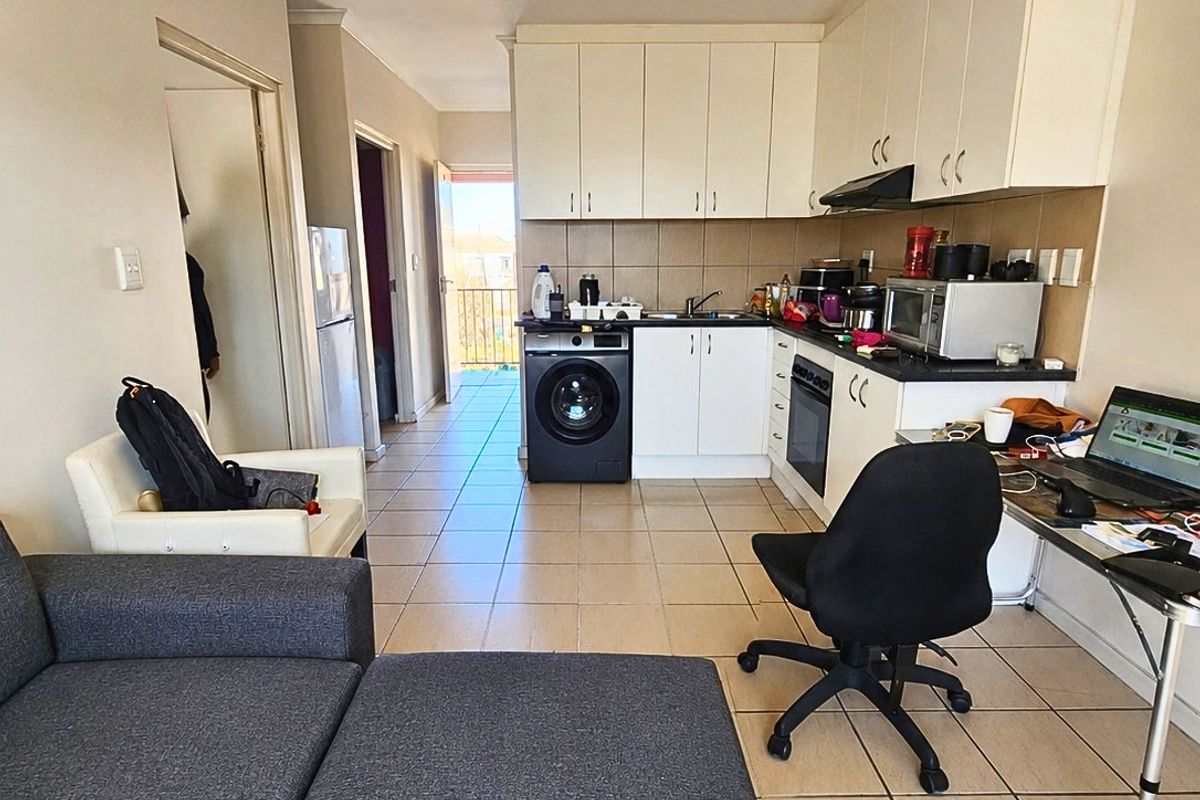 Open-plan living and kitchen area featuring tiled flooring, built-in cabinetry, integrated appliances, and direct access to a balcony.