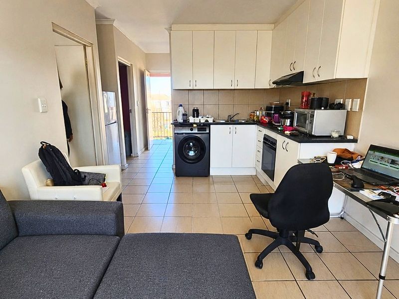 Open-plan living and kitchen area featuring tiled flooring, built-in cabinetry, integrated appliances, and direct access to a balcony.