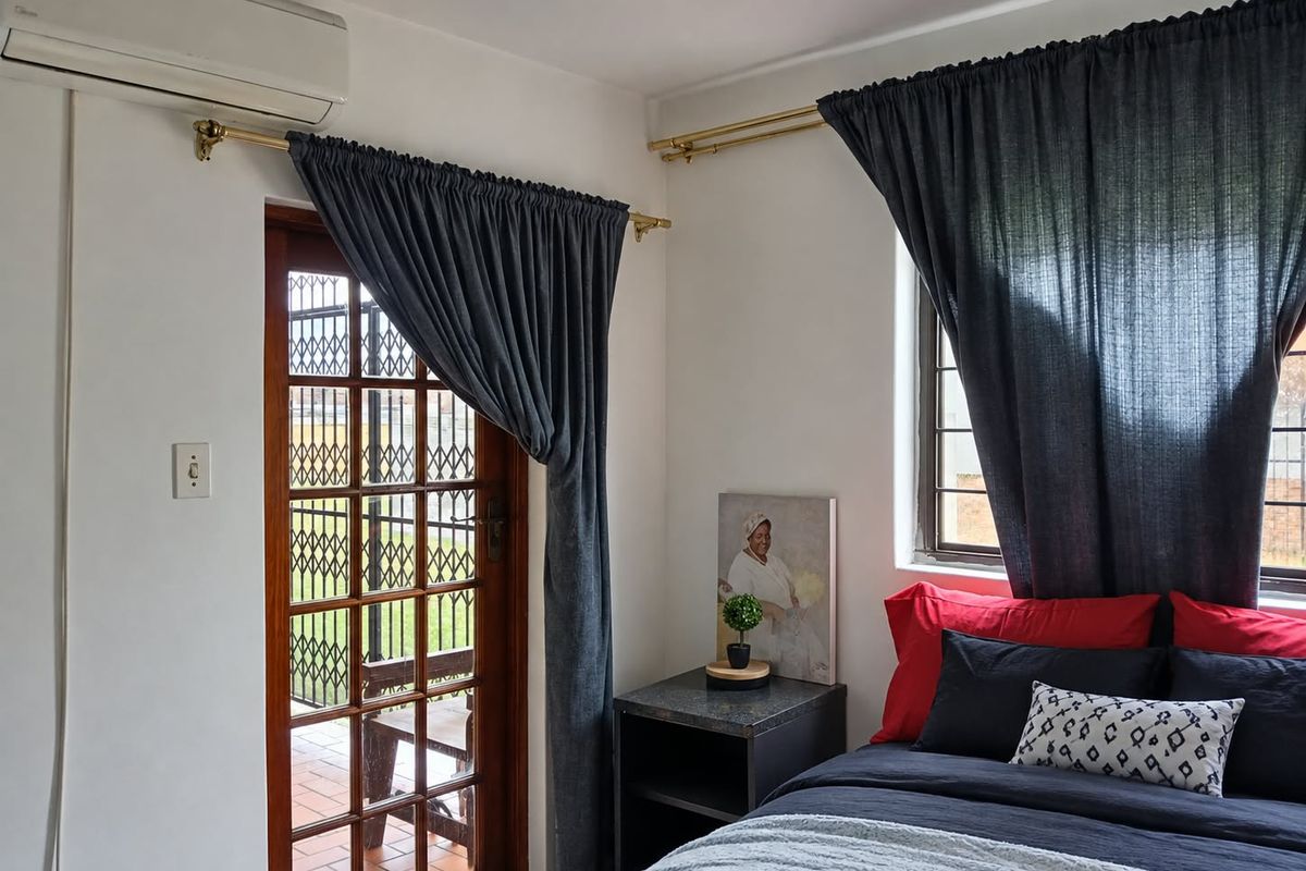 A well-maintained bedroom featuring a split-system air conditioner, timber-framed glass door with security gate, and a window with security bars.