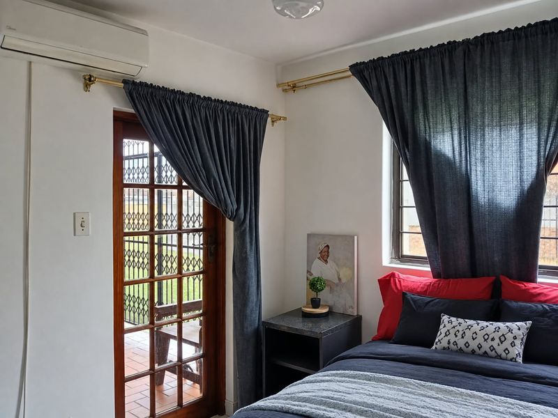 A well-maintained bedroom featuring a split-system air conditioner, timber-framed glass door with security gate, and a window with security bars.