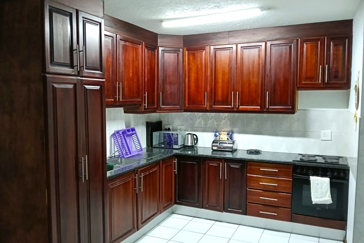 A functional kitchen featuring dark wood cabinetry, granite countertops, a built-in oven, and a tiled backsplash with white floor tiles.