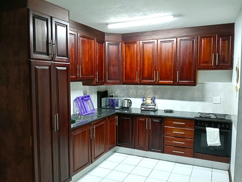 A functional kitchen featuring dark wood cabinetry, granite countertops, a built-in oven, and a tiled backsplash with white floor tiles.