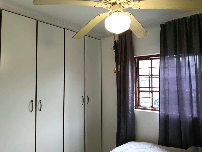 A bedroom featuring built-in cupboards, a ceiling fan, and a window fitted with security burglar bars.