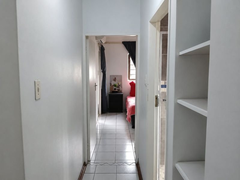 A functional hallway featuring tiled flooring and built-in shelving, providing access to adjacent rooms within the apartment.