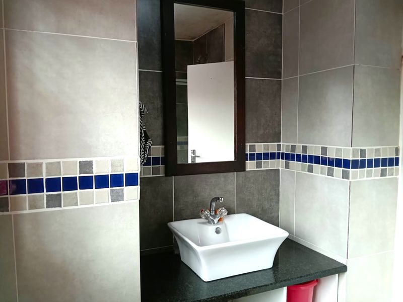 A clean bathroom vanity area featuring a modern white vessel sink, granite countertop, and decorative mosaic tile accents on the walls.