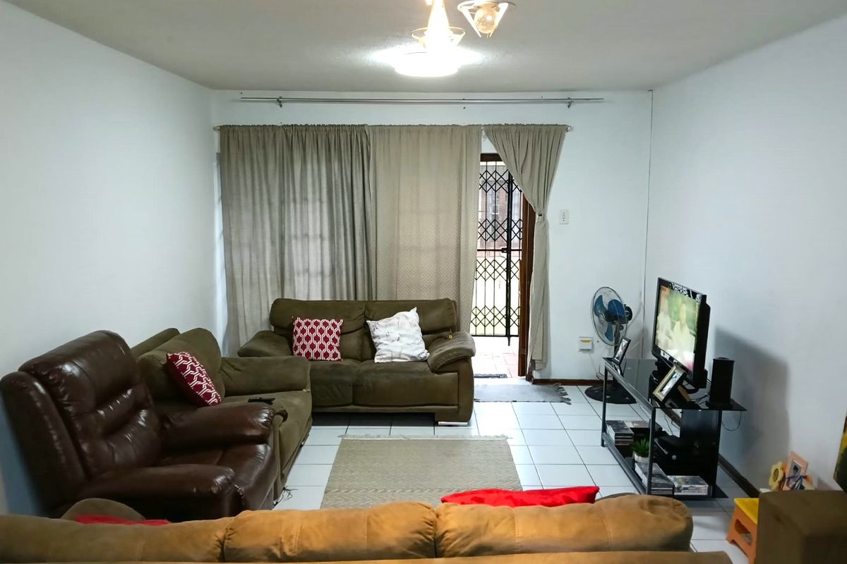 A living room featuring tiled flooring and a security gate leading to an outdoor area, providing a functional and accessible living space.