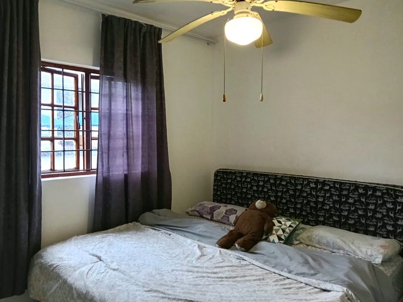A functional bedroom featuring a ceiling fan and a window fitted with security bars, providing natural light and ventilation.