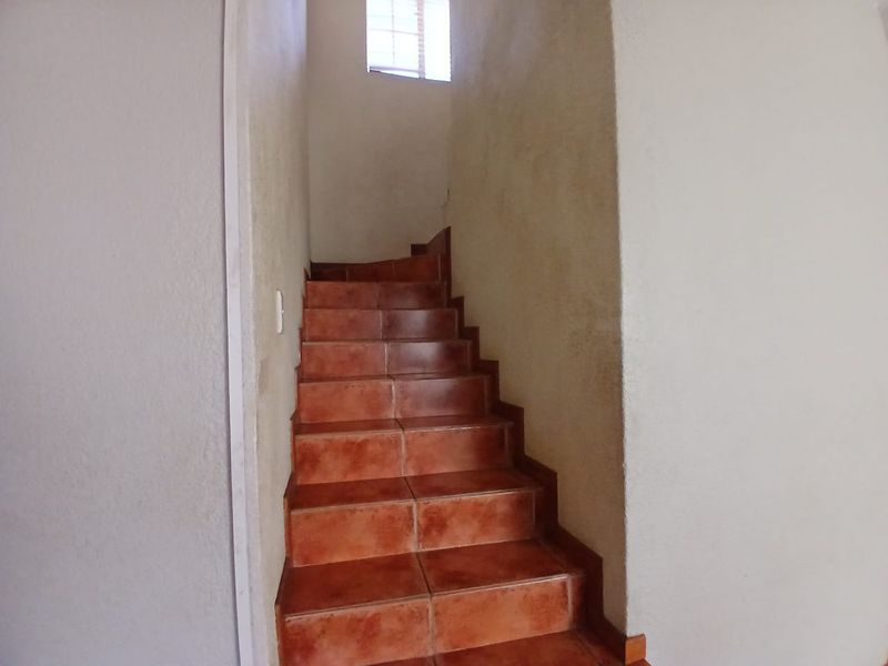 A simple interior staircase featuring terracotta-style floor tiles and plain walls, leading to an upper level with natural light from a small window.