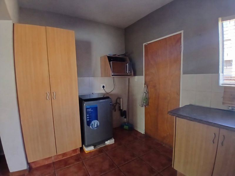 A functional laundry area featuring tiled flooring, built-in cabinetry, and tiled splashbacks, providing essential utility space for the apartment.