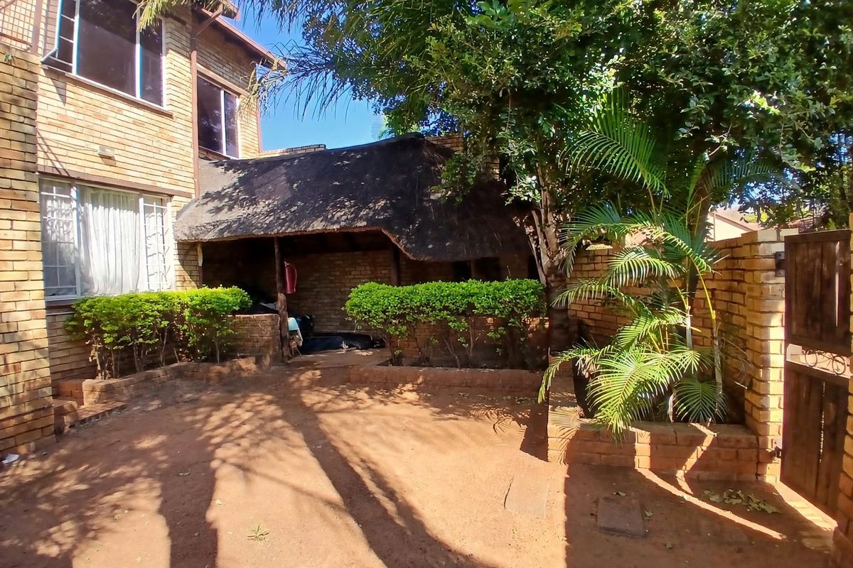 Rear exterior view featuring a face brick building, a thatched roof lapa, and a garden area with established trees and brick boundary walls.
