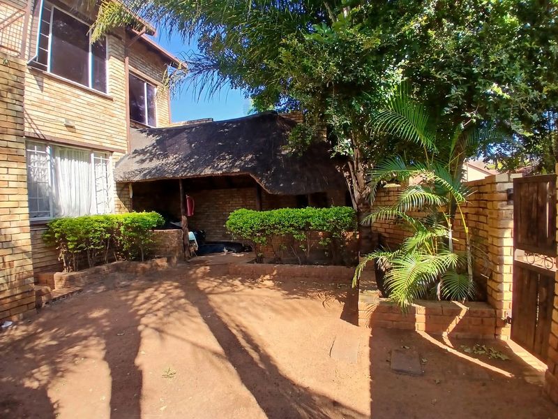 Rear exterior view featuring a face brick building, a thatched roof lapa, and a garden area with established trees and brick boundary walls.