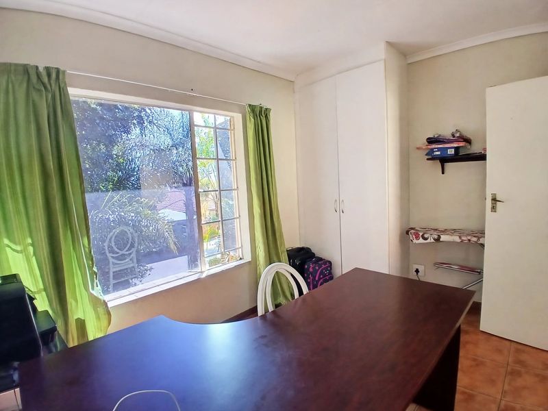 A functional bedroom featuring tiled flooring, a built-in wardrobe, and a large window providing natural light.