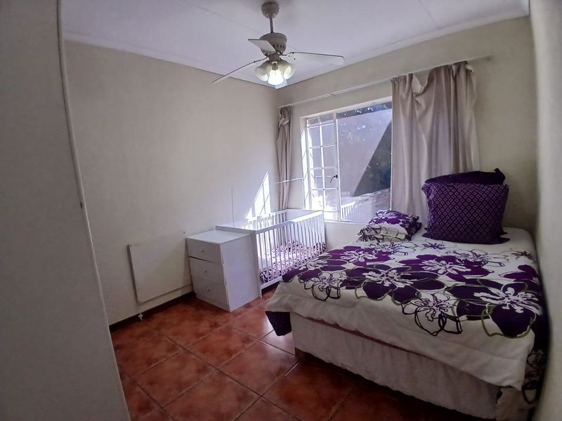 A bedroom featuring tiled flooring, a ceiling fan, and a window with security bars, providing a functional and well-lit living space.