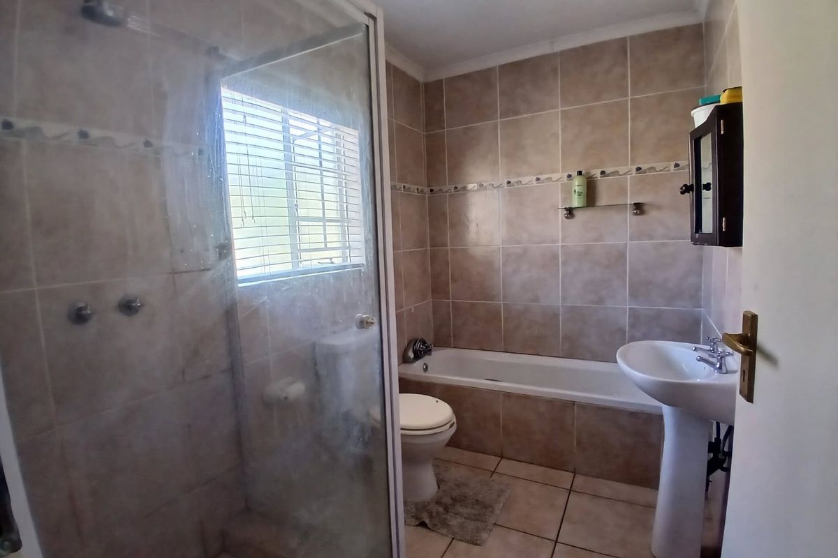 A functional bathroom featuring a shower enclosure, bathtub, pedestal basin, and toilet with neutral wall and floor tiling.