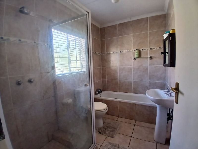 A functional bathroom featuring a shower enclosure, bathtub, pedestal basin, and toilet with neutral wall and floor tiling.