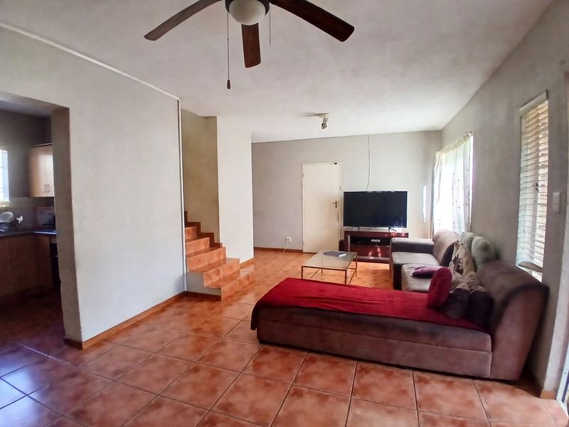 Open-plan living area featuring tiled flooring, a ceiling fan, and an adjoining staircase, providing a functional layout with direct access to the kitchen.