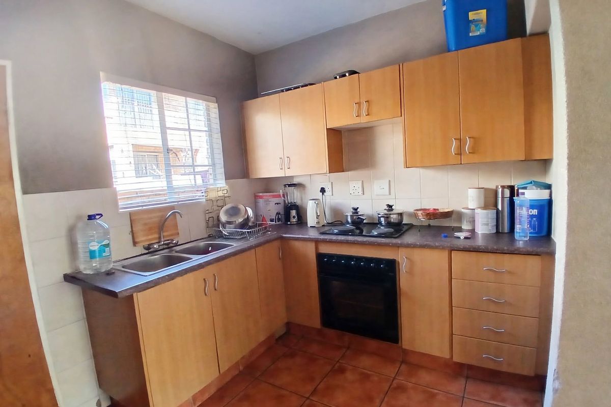 A functional kitchen featuring light wood-tone cabinetry, laminate countertops, a built-in oven with electric hob, and durable ceramic floor tiles.
