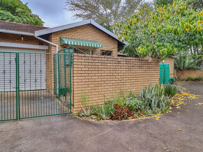 Front exterior view of a face brick townhouse featuring a garage, secure gated entrance, and established garden area.