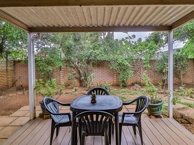Covered outdoor patio featuring timber decking and a corrugated metal roof, overlooking a private garden enclosed by a brick boundary wall.