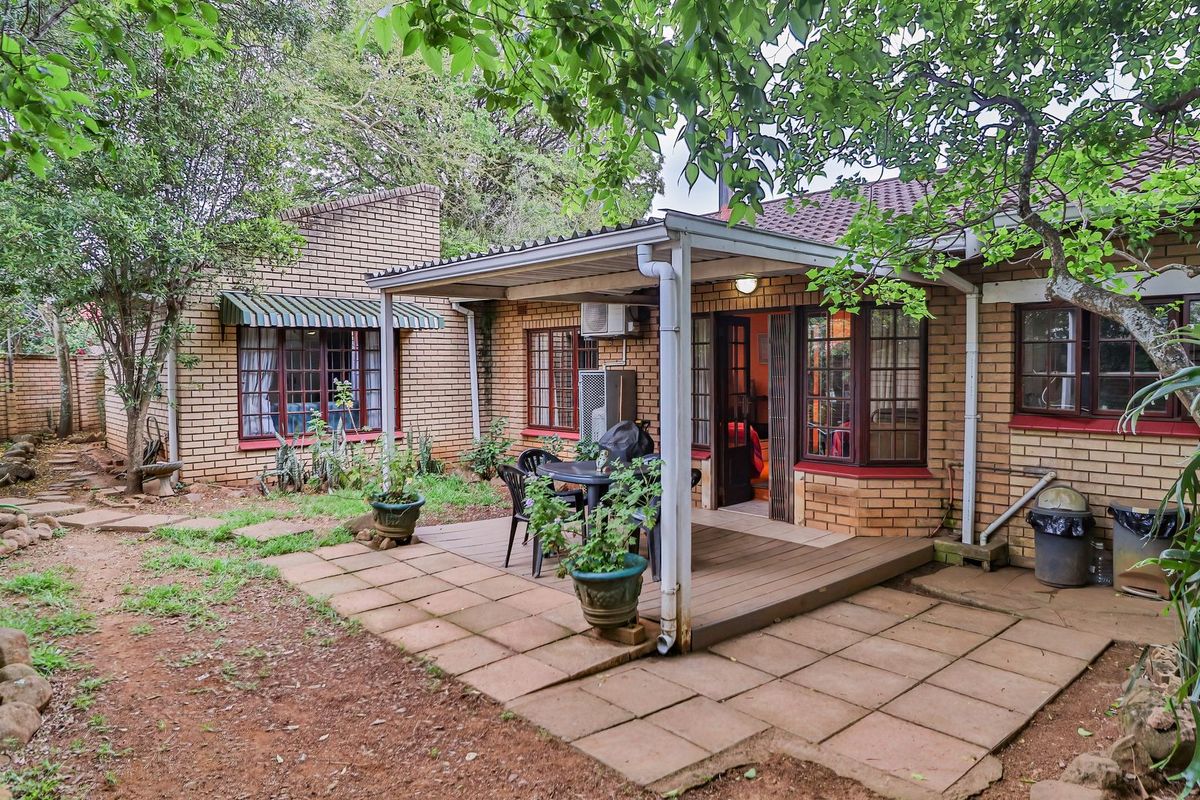 A rear exterior view of the townhouse featuring a brick facade, a covered patio area with timber decking, and a surrounding garden space.