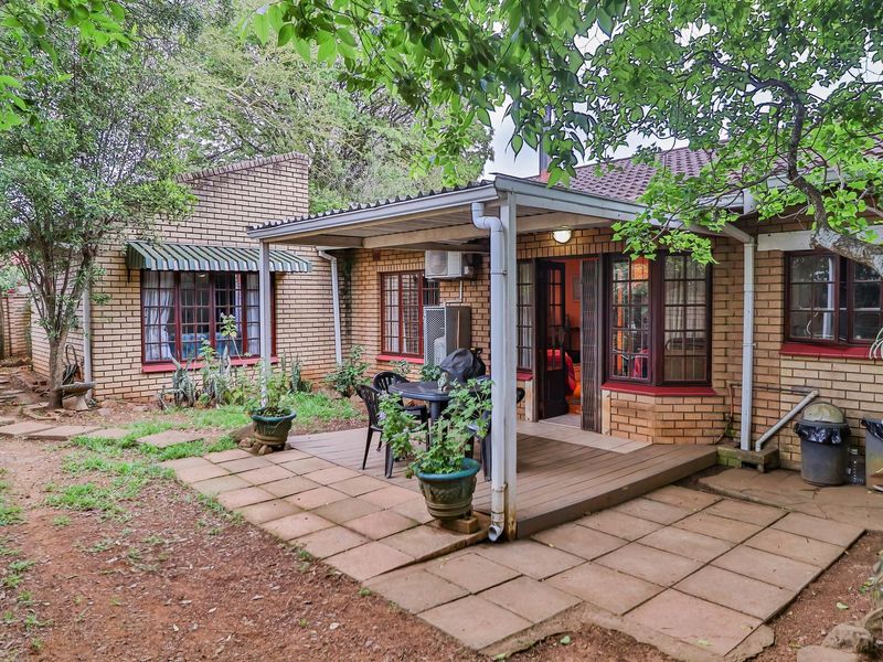 A rear exterior view of the townhouse featuring a brick facade, a covered patio area with timber decking, and a surrounding garden space.