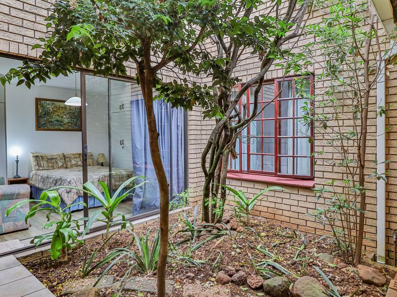 A private rear courtyard featuring a brick facade, established garden beds, and direct access to the interior through a sliding glass door.