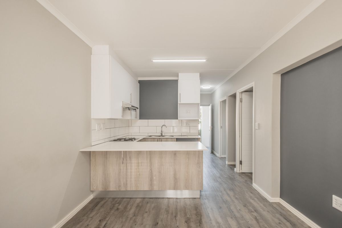 Modern open-plan kitchen featuring light wood-finish cabinetry, white countertops, a gas hob, and a tiled backsplash, leading into a hallway.