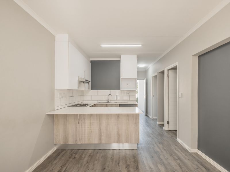 Modern open-plan kitchen featuring light wood-finish cabinetry, white countertops, a gas hob, and a tiled backsplash, leading into a hallway.