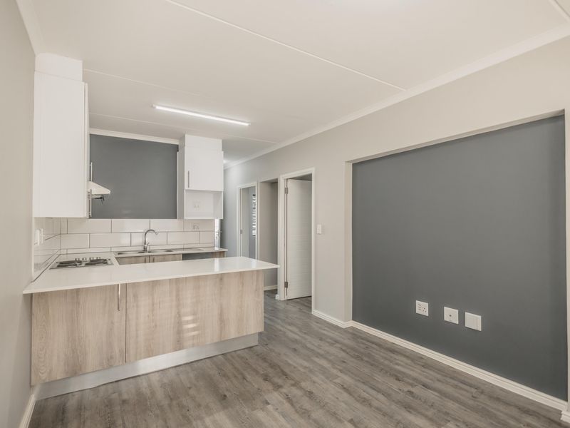 Modern open-plan kitchen and living area featuring light wood cabinetry, a breakfast bar, and durable laminate flooring in a clean, neutral setting.