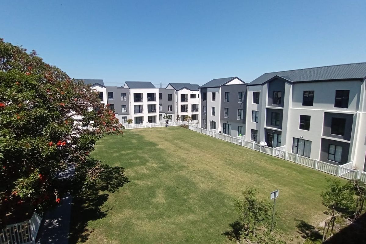 A view of the communal garden area and rear facades of the modern apartment complex, featuring well-maintained lawns and secure fencing.