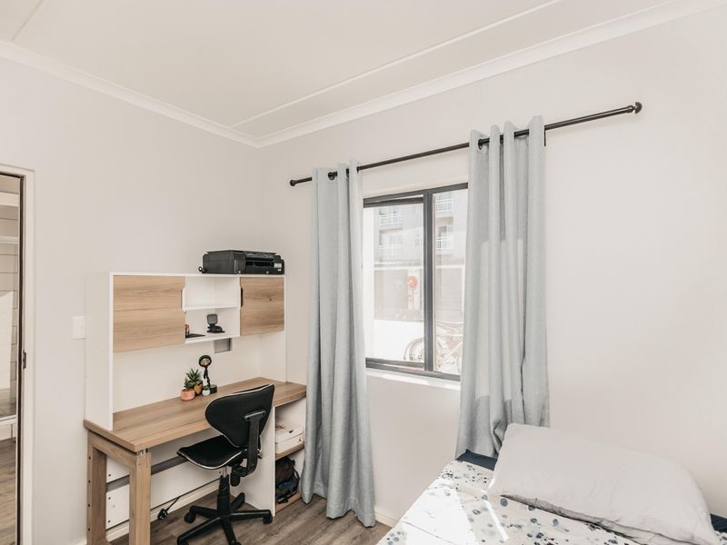 A well-maintained bedroom featuring laminate flooring, cove cornicing, and a built-in desk unit, with natural light provided by an aluminium-framed window.