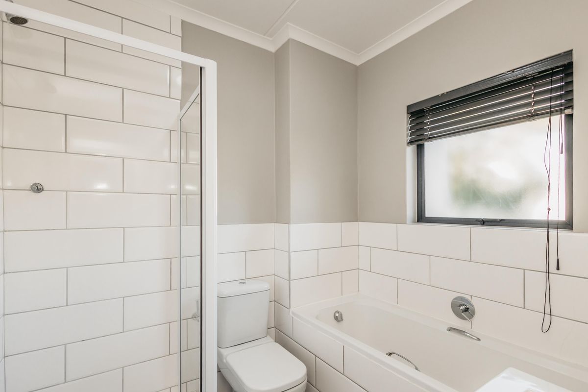 A clean, modern bathroom featuring a glass-enclosed shower, a built-in bathtub, and classic white subway tile wall finishes.